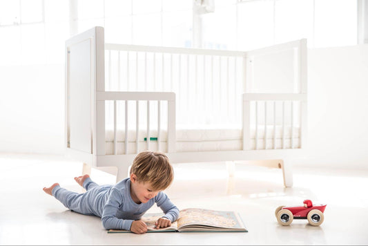 Young kid reading on the floor near his 4-in-1-crib