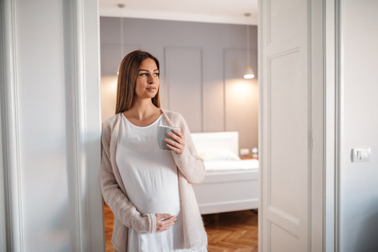 Pregnant woman drinking tea and holding belly in door way