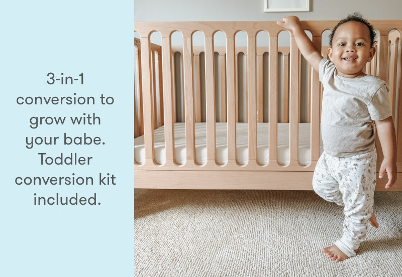 toddler standing next to newton galileo crib in natural color, text reads "3-in-1 conversion to grow with your babe. Toddler conversion kit included."